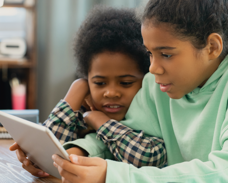 Two primary school reading together on a tablet device at home