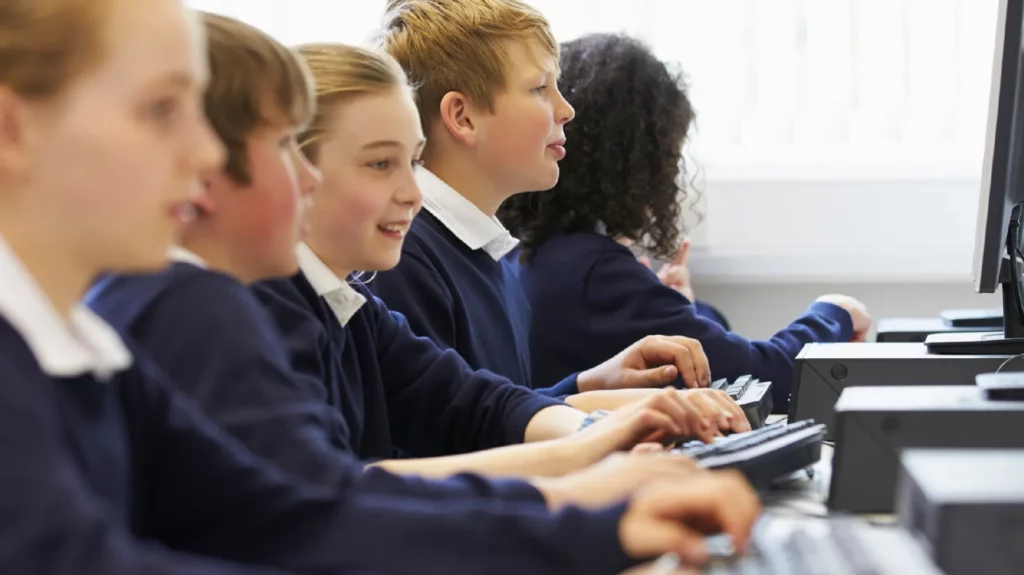 Five children wearing school uniform sitting in class and using desktop computers to access their school work