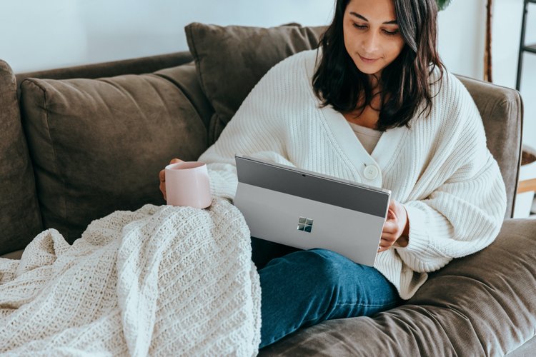 Cosy woman sitting under a blanket on a couch reading an ebook on a tablet device