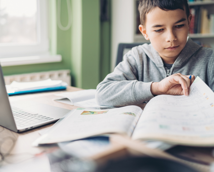 Homeschooled child paging through a workbook and accessing his school resources via Snapplify on a laptop