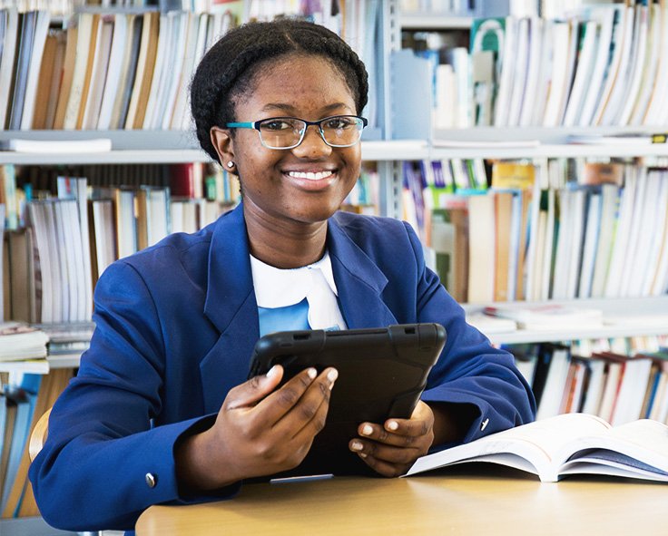 A teenager in at the library in school uniform accessing her school work using Snapplify on a tablet device